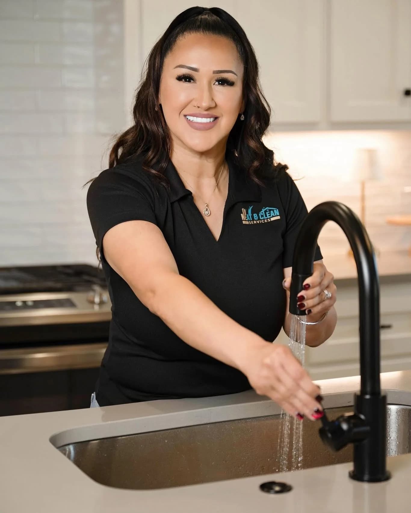 Stephanie Perez, founder of Neat & Clean Services, in a branded polo at a kitchen sink